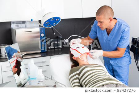 Cosmetologist performing face phototherapy procedure for female client Cosmetologist performing face phototherapy procedure for female client 88427276