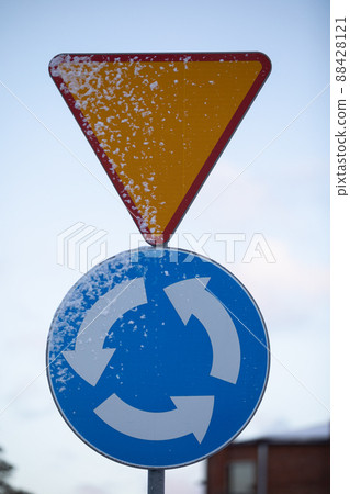 Snowy road sign, intersection with circular traffic. 88428121