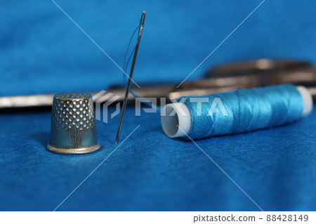 Spool of Blue Thread, Thimble and Needle on Blue Fabric 88428149