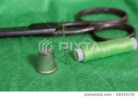 Spool of Green Thread, Thimble and Needle on Green Fabric 88428150