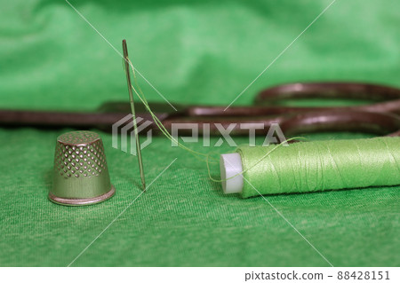 Spool of Green Thread, Thimble and Needle on Green Fabric 88428151