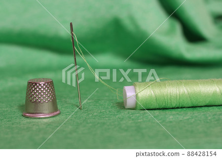 Spool of Green Thread, Thimble and Needle on Green Fabric 88428154
