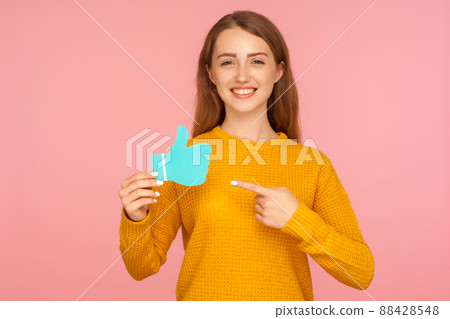Like and share. Portrait of attractive happy red hair girl in sweater pointing at blue thumb up love icon and smiling, social media recommendation, blogging. studio shot isolated on pink background Like and share. Portrait of attractive happy red hair girl in sweater pointing at blue thumb up love icon and smiling, social media recommendation, blogging. studio shot isolated on pink background 88428548