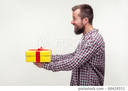 Take this present. Side view portrait of kind-hearted bearded man in casual plaid shirt giving gift box, smiling looking friendly and generous, charity. indoor studio shot isolated on white background Take this present. Side view portrait of kind-hearted bearded man in casual plaid shirt giving gift box, smiling looking friendly and generous, charity. indoor studio shot isolated on white background 88428551