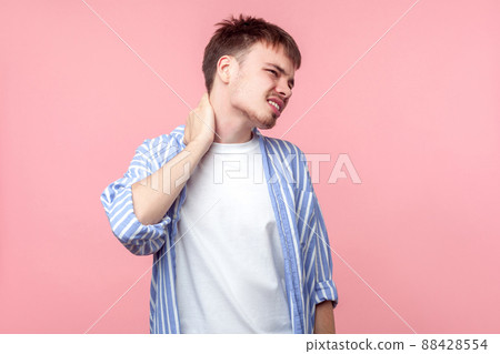 Strong neck pain. Portrait of tired brown-haired man with small beard and mustache in casual shirt massaging neck, employer suffering muscle strain. indoor studio shot isolated on pink background Strong neck pain. Portrait of tired brown-haired man with small beard and mustache in casual shirt massaging neck, employer suffering muscle strain. indoor studio shot isolated on pink background 88428554