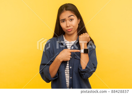 Time to go, hurry up. Portrait of displeased angry woman in denim shirt looking impatient and pointing wristwatch, warning of deadline, late hour. indoor studio shot isolated on yellow background Time to go, hurry up. Portrait of displeased angry woman in denim shirt looking impatient and pointing wristwatch, warning of deadline, late hour. indoor studio shot isolated on yellow background 88428837