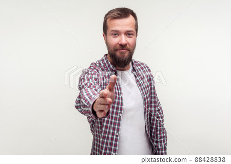 Portrait of friendly bearded young man in casual plaid shirt standing giving hand to handshake, getting acquainted at job interview, meeting new people. indoor studio shot isolated on white background Portrait of friendly bearded young man in casual plaid shirt standing giving hand to handshake, getting acquainted at job interview, meeting new people. indoor studio shot isolated on white background 88428838