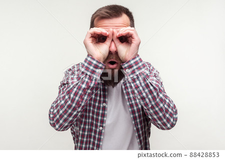 Portrait of curious wondered bearded man in casual plaid shirt looking through fingers gesturing binoculars, amazed surprised by what he discovers. indoor studio shot isolated on white background Portrait of curious wondered bearded man in casual plaid shirt looking through fingers gesturing binoculars, amazed surprised by what he discovers. indoor studio shot isolated on white background 88428853