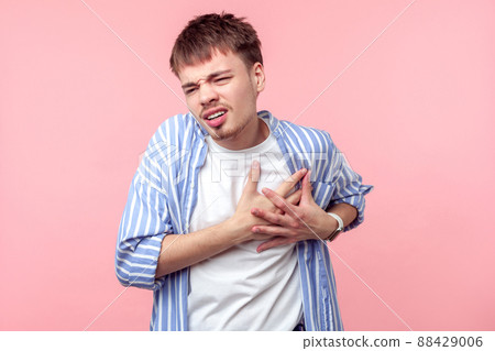 Heart attack. Portrait of sick brown-haired man with small beard and mustache in casual shirt clutching chest suffering acute pain, risk of infarction. indoor studio shot isolated on pink background Heart attack. Portrait of sick brown-haired man with small beard and mustache in casual shirt clutching chest suffering acute pain, risk of infarction. indoor studio shot isolated on pink background 88429006