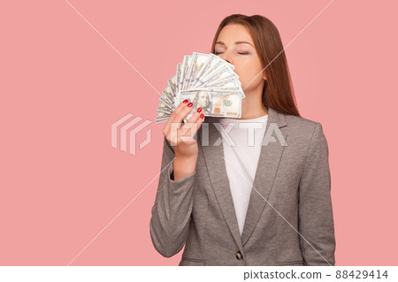 Greedy for money. Portrait of businesswoman in suit jacket smelling dollar banknotes with expression of pleasure, enjoying financial success, wealth. indoor studio shot isolated on pink background Greedy for money. Portrait of businesswoman in suit jacket smelling dollar banknotes with expression of pleasure, enjoying financial success, wealth. indoor studio shot isolated on pink background 88429414