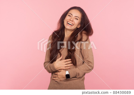 Humor and laughter. Portrait of happy beautiful young woman with brunette wavy hair holding her belly and laughing out loud at hilarious anecdote, funny joke. studio shot isolated on pink background 88430089