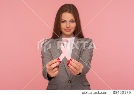 Female health, medical insurance. Portrait of young positive businesswoman in elegant suit jacket holding pink ribbon, warning of breast cancer risk and society awareness. studio shot, pink background Female health, medical insurance. Portrait of young positive businesswoman in elegant suit jacket holding pink ribbon, warning of breast cancer risk and society awareness. studio shot, pink background 88430179