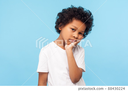 Portrait of lazy bored preschool boy with curly hair leaning on hand and looking depressed, child with indifferent gloomy expression has no energy. indoor studio shot isolated on blue background Portrait of lazy bored preschool boy with curly hair leaning on hand and looking depressed, child with indifferent gloomy expression has no energy. indoor studio shot isolated on blue background 88430224