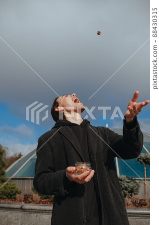 Young gay hipster eating peanuts at the street smiling happy sunglasses Young gay hipster eating peanuts at the street smiling happy sunglasses 88430315