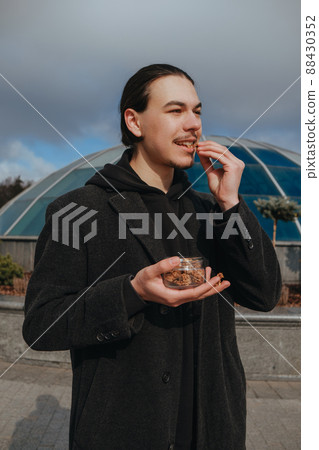 Young gay hipster eating peanuts at the street smiling happy sunglasses Young gay hipster eating peanuts at the street smiling happy sunglasses 88430352