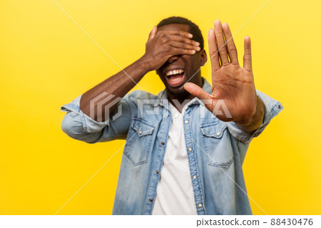 No, I don't want to watch. Portrait of scared panicked man in denim casual shirt standing with covered eyes and showing stop gesture, afraid to look. indoor studio shot isolated on yellow background 88430476