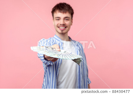 Portrait of successful rich brunette man with small beard and mustache in casual shirt proposing dollars to camera, giving big sun of money, investment. indoor studio shot isolated on pink background Portrait of successful rich brunette man with small beard and mustache in casual shirt proposing dollars to camera, giving big sun of money, investment. indoor studio shot isolated on pink background 88430477