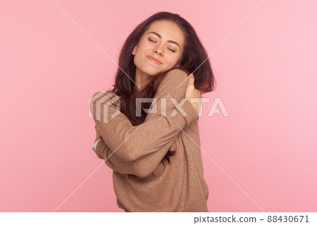 I am egoist, love myself. Portrait of selfish narcissistic young woman with brunette hair embracing herself and smiling with dreamy satisfied expression. indoor studio shot isolated on pink background 88430671