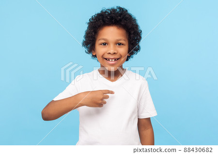 This is me. Portrait of happy preschool curly boy in T-shirt joyfully looking at camera and pointing to himself, proud of own success, egoistic child. indoor studio shot isolated on blue background This is me. Portrait of happy preschool curly boy in T-shirt joyfully looking at camera and pointing to himself, proud of own success, egoistic child. indoor studio shot isolated on blue background 88430682
