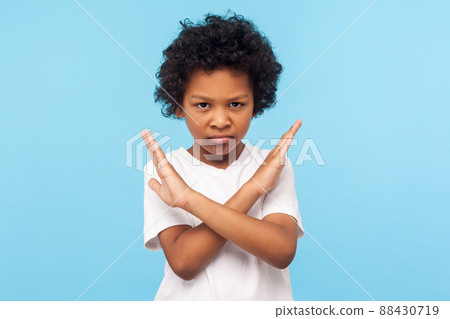 Stop, I'm warning. Portrait of angry determined little boy with curls crossing hands and looking at camera with aggression, showing stop gesture, way prohibited. indoor studio shot blue background Stop, I'm warning. Portrait of angry determined little boy with curls crossing hands and looking at camera with aggression, showing stop gesture, way prohibited. indoor studio shot blue background 88430719
