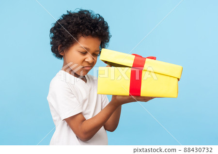Portrait of curious adorable little boy peeking inside gift box, unpacking present with funny inquisitive look, impatient child unboxing birthday surprise. studio shot isolated on blue background 88430732