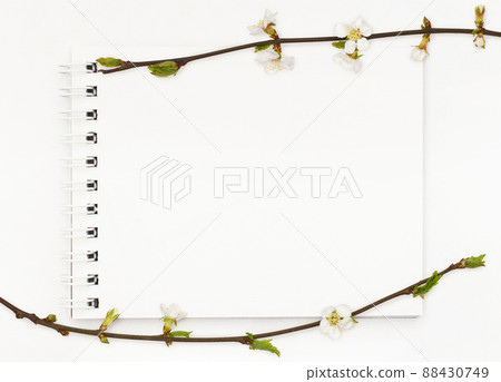 Notepad with white empty page and spring frame with twigs of small flowers and leaves on white background. Flat lay. Notepad with white empty page and spring frame with twigs of small flowers and leaves on white background. Flat lay. 88430749