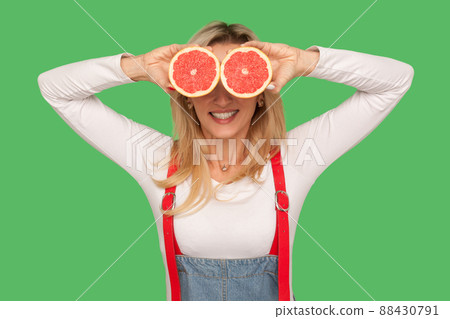 Fresh fruits, natural organic food. Portrait of happy stylish woman covering eyes with sliced juicy grapefruits and smiling, vitamins for healthy diet. indoor studio shot isolated on green background 88430791