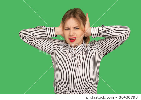Don't want to listen anymore. Angry irritated blond girl in blouse covering ears with hands to stop hear annoying talk, avoiding high-decibel sound. indoor studio shot isolated on green background Don't want to listen anymore. Angry irritated blond girl in blouse covering ears with hands to stop hear annoying talk, avoiding high-decibel sound. indoor studio shot isolated on green background 88430798