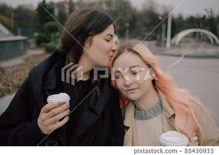Young ukrainian lesbian couple kissing each other at the street with coffee Young ukrainian lesbian couple kissing each other at the street with coffee 88430933