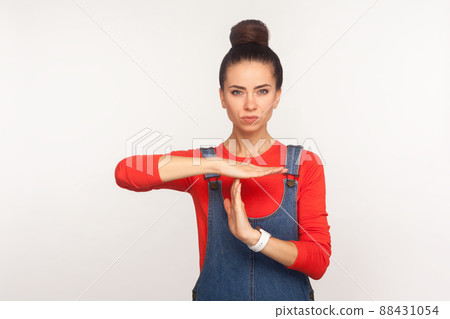 I need break. Portrait of tired displeased girl with hair bun in denim overalls showing time out gesture and looking with dissatisfied expression. indoor studio shot isolated on white background 88431054