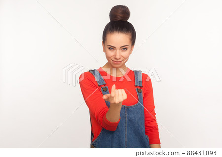 Come here, handsome. Portrait of attractive stylish girl with hair bun in denim overalls inviting with beckoning gesture and looking alluring seductive. indoor studio shot isolated on white background 88431093