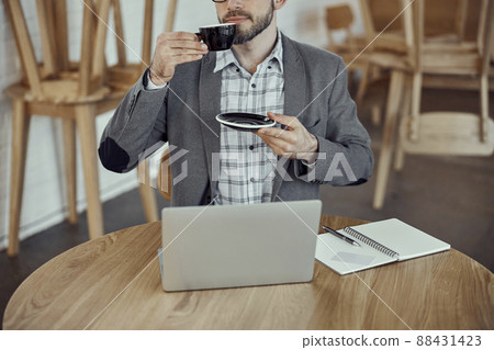 Young man drinking coffee and using notebook in cafe Young man drinking coffee and using notebook in cafe 88431423