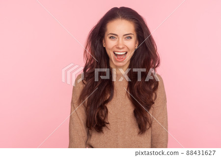 Portrait of delighted young woman with long brunette wavy hair looking at camera with extremely happy joyful smile, expressing optimism, positive emotions. studio shot isolated on pink background 88431627