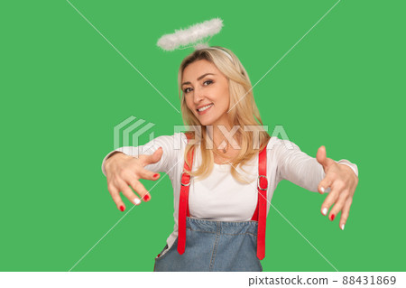 Kindness and generosity. Portrait of angelic beautiful adult woman with nimbus above head holding outstretched hands and smiling, giving free hugs. indoor studio shot isolated on green background 88431869