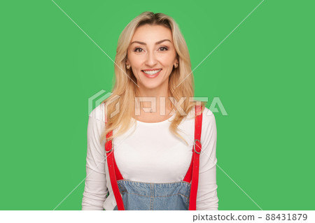 Portrait of happy joyful beautiful adult blond woman in stylish denim overalls looking at camera with toothy smile, friendly optimistic expression. indoor studio shot isolated on green background Portrait of happy joyful beautiful adult blond woman in stylish denim overalls looking at camera with toothy smile, friendly optimistic expression. indoor studio shot isolated on green background 88431879