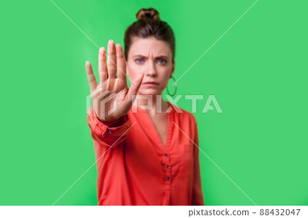 Stop, no. Portrait of angry or worried young woman with bun hairstyle, big earrings and in red blouse frowning gesturing caution to camera, prohibition. indoor studio shot isolated on green background Stop, no. Portrait of angry or worried young woman with bun hairstyle, big earrings and in red blouse frowning gesturing caution to camera, prohibition. indoor studio shot isolated on green background 88432047
