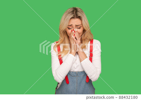 Portrait of upset adult woman in denim overalls crying from sadness, suffering depression and loneliness, negative emotions, frustrated by misfortune. indoor studio shot isolated on green background Portrait of upset adult woman in denim overalls crying from sadness, suffering depression and loneliness, negative emotions, frustrated by misfortune. indoor studio shot isolated on green background 88432180