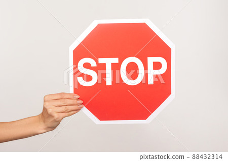 Closeup of female hand holding octagonal Stop symbol, ban concept, arm showing red traffic sign warning of forbidden way, restricted area, prohibited to go. studio shot isolated on blue background 88432314