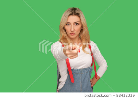 Are you ready. Portrait of serious adult blond woman in stylish denim overalls pointing finger to camera, noticing and choosing with bossy expression. indoor studio shot isolated on green background Are you ready. Portrait of serious adult blond woman in stylish denim overalls pointing finger to camera, noticing and choosing with bossy expression. indoor studio shot isolated on green background 88432339