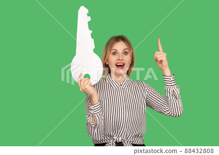 Excited pretty girl with red lips in glamour striped blouse pointing finger up with excellent idea and holding big key, found genius solution. indoor studio shot isolated on green background Excited pretty girl with red lips in glamour striped blouse pointing finger up with excellent idea and holding big key, found genius solution. indoor studio shot isolated on green background 88432808