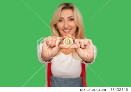 Look at digital money. Portrait of happy adult blond woman with charming smile holding golden bitcoin, showing btc coin and expressing optimism, joy. indoor studio shot isolated on green background Look at digital money. Portrait of happy adult blond woman with charming smile holding golden bitcoin, showing btc coin and expressing optimism, joy. indoor studio shot isolated on green background 88432846