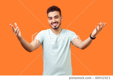 Come and give me hug. Portrait of positive generous brunette man with beard in casual white t-shirt holding hands raised and wide opened to embrace. indoor studio shot isolated on orange background Come and give me hug. Portrait of positive generous brunette man with beard in casual white t-shirt holding hands raised and wide opened to embrace. indoor studio shot isolated on orange background 88432921