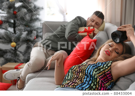 Young woman suffering from hangover and man sleeping on sofa at home after New Year party Young woman suffering from hangover and man sleeping on sofa at home after New Year party 88433004