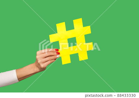 Blog comments, social media trends. Closeup of woman hand holding big yellow hashtag sign, tagging famous internet post, sharing viral content, popular idea. studio shot isolated on green background 88433330