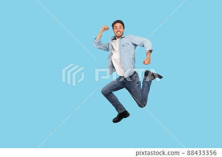 Full length, man in denim outfit flying and jumping in air with inspired ambitious expression, taking big step and hurrying, running to final sale. indoor studio shot isolated on blue background Full length, man in denim outfit flying and jumping in air with inspired ambitious expression, taking big step and hurrying, running to final sale. indoor studio shot isolated on blue background 88433356
