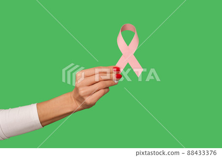 Closeup of tiny female hand with manicure holding pink ribbon, symbol of breast cancer awareness, oncological disease prevention and female healthcare. indoor studio shot isolated on green background Closeup of tiny female hand with manicure holding pink ribbon, symbol of breast cancer awareness, oncological disease prevention and female healthcare. indoor studio shot isolated on green background 88433376