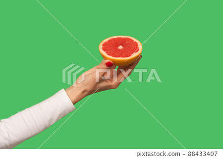 Closeup of hand holding sliced juicy grapefruit, tasty fruit for detox, natural organic vegetarian food full with vitamins, healthy diet and weightloss concept. indoor, isolated on green background Closeup of hand holding sliced juicy grapefruit, tasty fruit for detox, natural organic vegetarian food full with vitamins, healthy diet and weightloss concept. indoor, isolated on green background 88433407