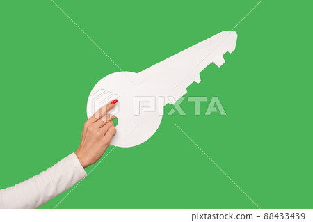 Closeup of woman hand holding big white house key, real estate advertisement, house purchase, key as metaphor of found solution and accessibility. indoor studio shot isolated on green background 88433439