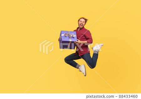 Enthusiastic extremely joyful hipster guy jumping trampoline with gift box, flying in air holding birthday present surprise, enjoying holiday bonus. full length studio shot isolated, yellow background Enthusiastic extremely joyful hipster guy jumping trampoline with gift box, flying in air holding birthday present surprise, enjoying holiday bonus. full length studio shot isolated, yellow background 88433460