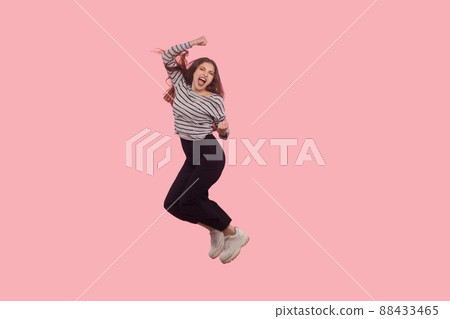 Life energy, freedom. Portrait of enthusiastic, extremely happy woman shouting for joy and flying, jumping in air with raised fists, celebrating success, victory. studio shot isolated, full length Life energy, freedom. Portrait of enthusiastic, extremely happy woman shouting for joy and flying, jumping in air with raised fists, celebrating success, victory. studio shot isolated, full length 88433465